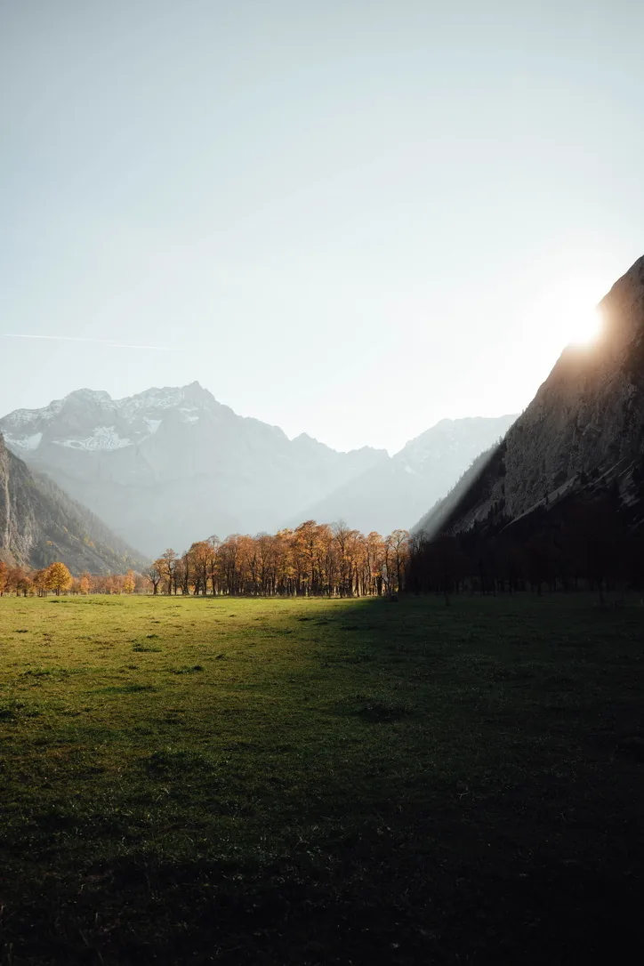 Sonnenlicht fällt über eine Wiese vor schroffen Berggipfeln.