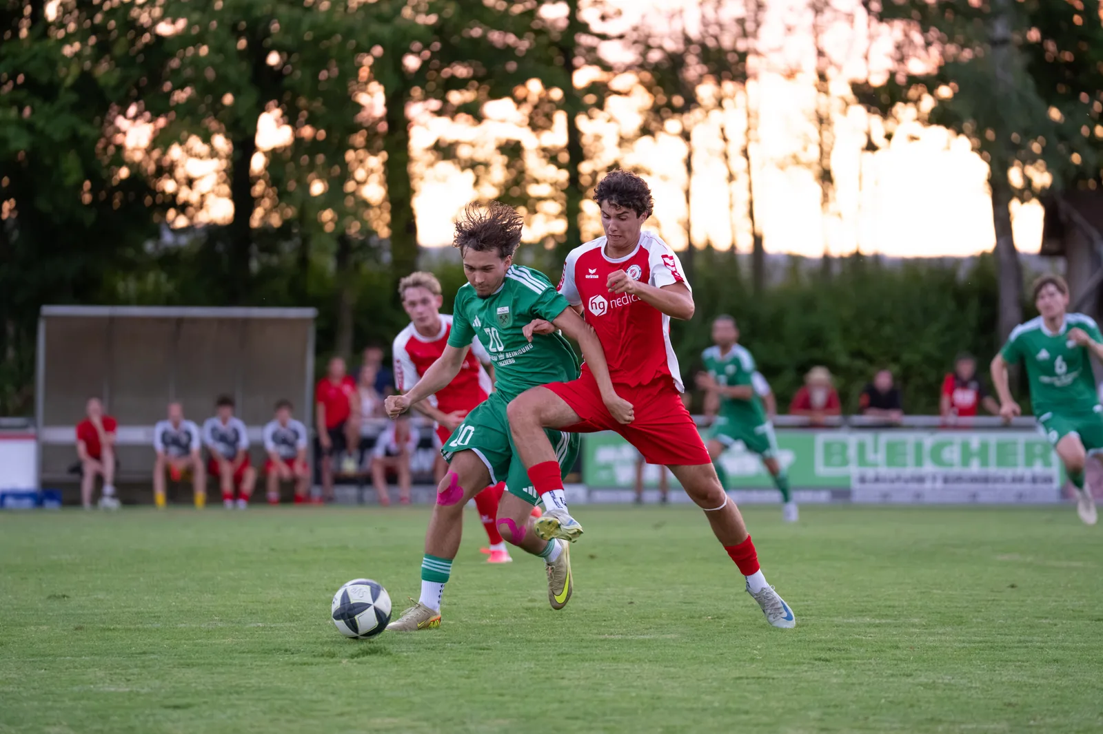 Zwei Fußballspieler in roten und grünen Trikots springen zum Kopfball.